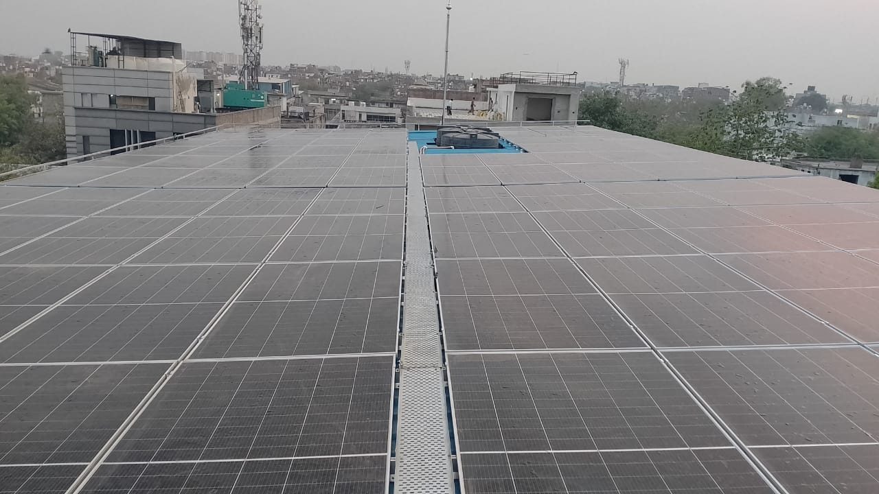 Solar panels on the raised shed roof at Arihant Cold Storage with the Okhla Phase II skyline behind
