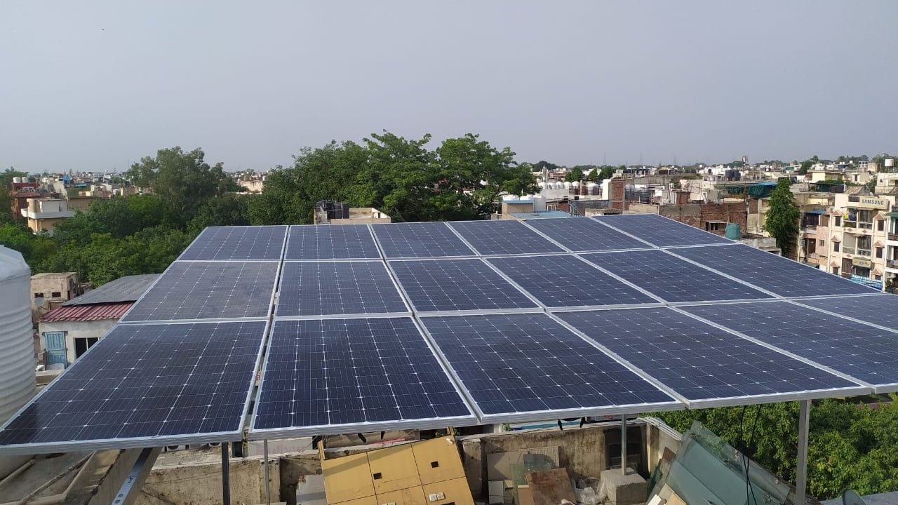 Elevated 20 kW rooftop solar array on a steel structure above a hotel building in Lajpat Nagar II, with the South Delhi skyline behind