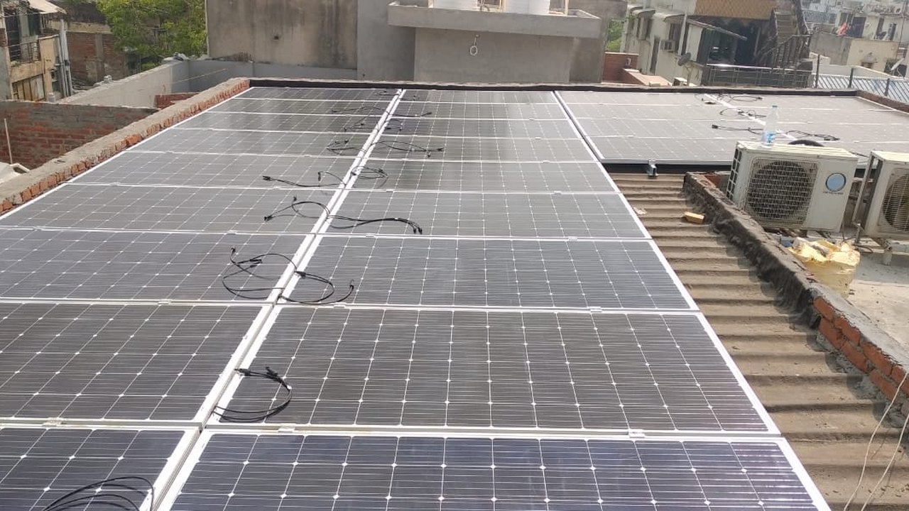 Solar modules mounted flat on the tin sheet roof of the Lajpat Nagar hotel, with the elevated section of the array beyond