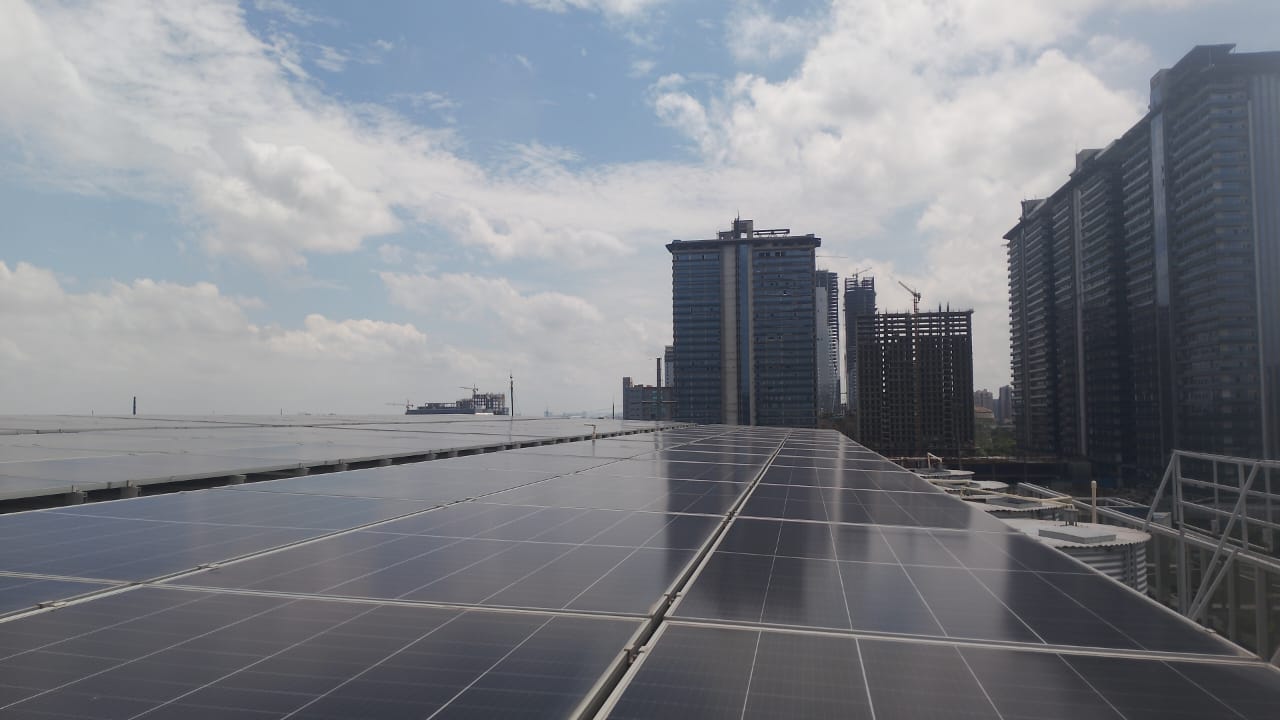 Solar panels on the fifth-floor raised shed roof at Steadfast Limited, with Noida high-rise towers in the background